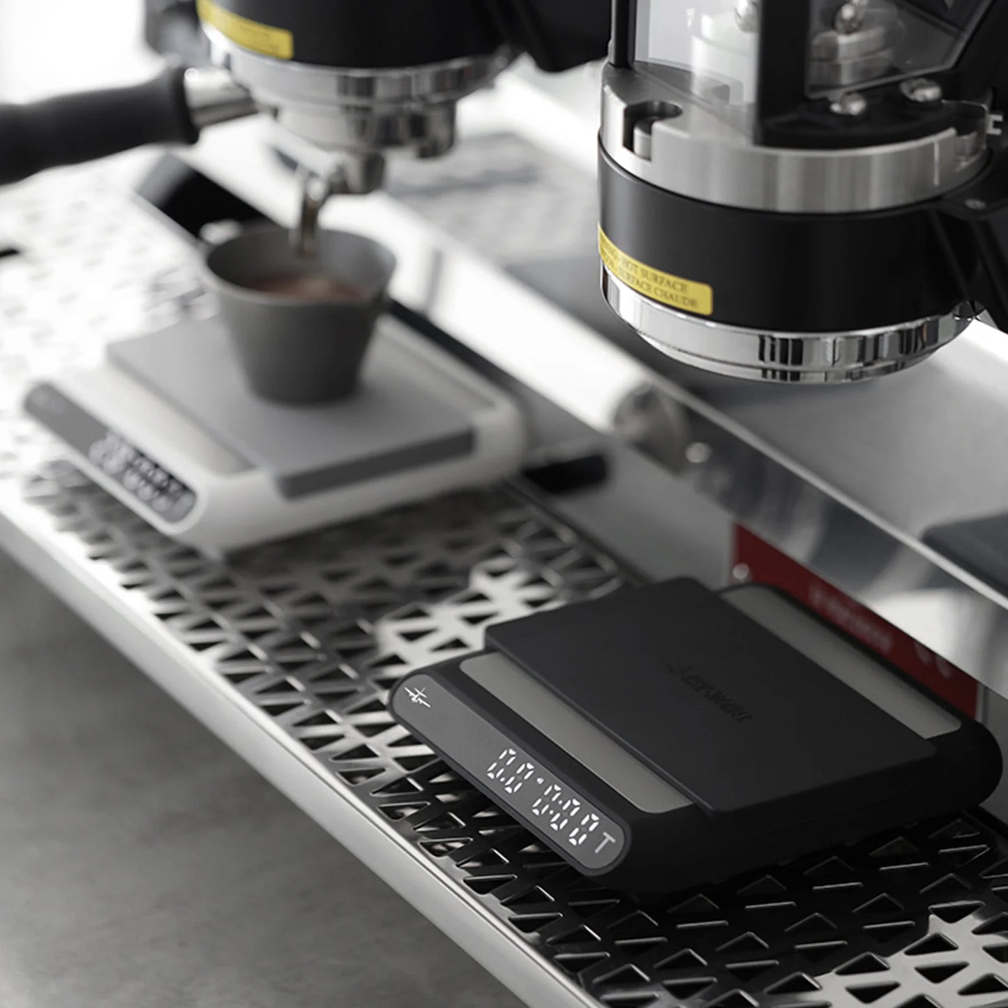 MHW-3BOMBER smart coffee scale. Black, with digital display on a stainless steel espresso machine.