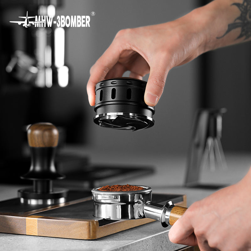 MHW-3BOMBER Falcon coffee distributor above portafilter. Black, stainless steel espresso tool on kitchen counter.