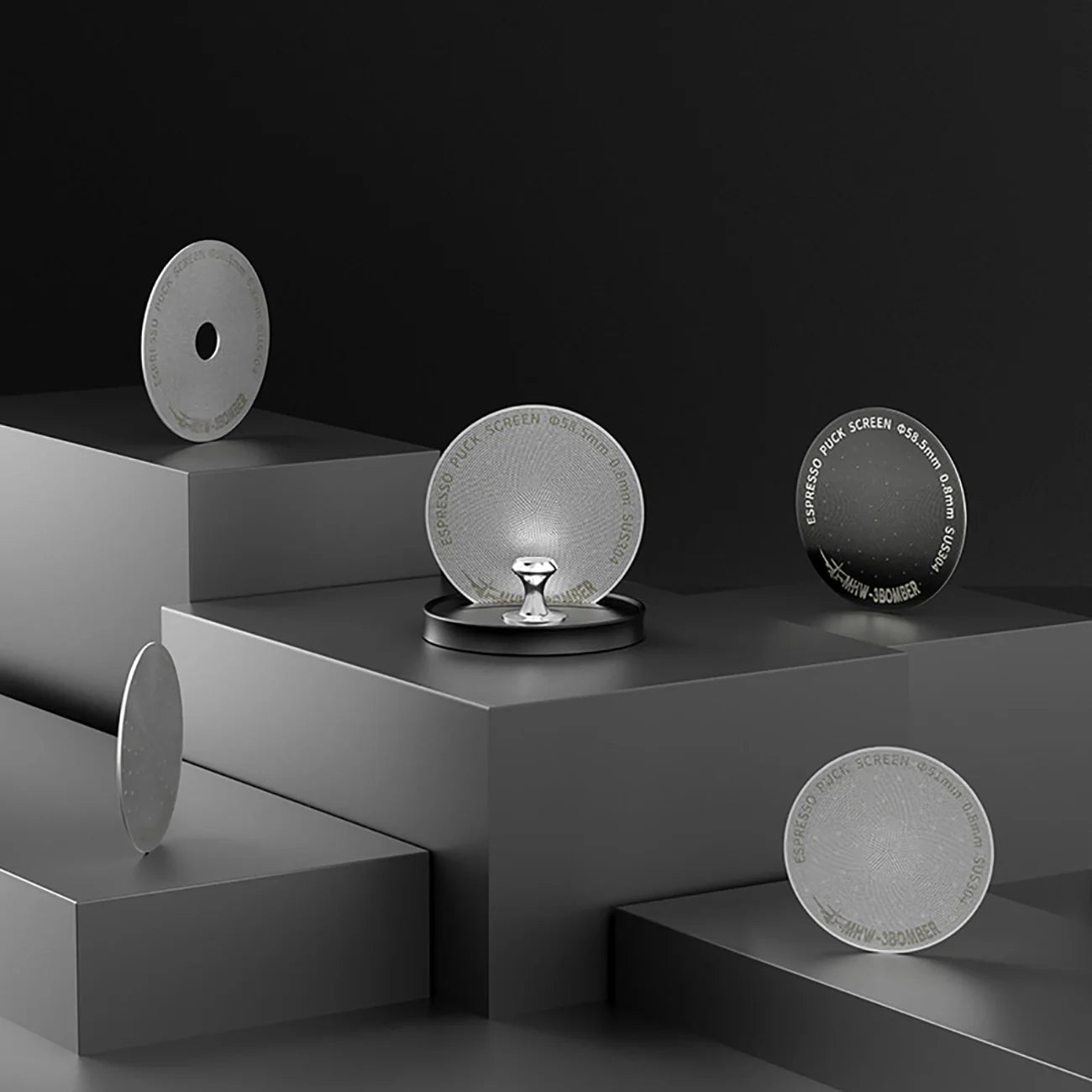 The MHW-3BOMBER Espresso Puck Screen Stand 51-58mm features a minimalist display with five textured gray disks on a multi-level black platform. A small metallic stand supports the central disk, while its magnetic design enhances user experience against the sleek dark gray backdrop.