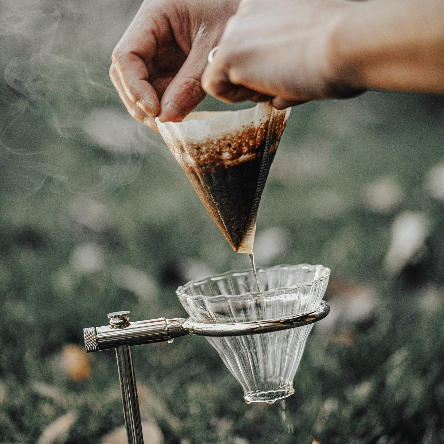 MHW-3BOMBER cone coffee paper filter in use with a clear glass dripper. Outdoor shot.