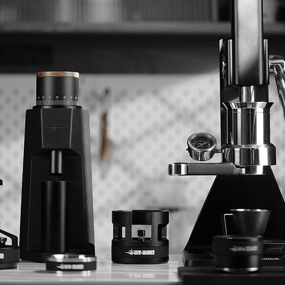 MHW-3BOMBER coffee setup: grinder, portafilter holder, and lever espresso machine. Black and silver, professional barista tools.