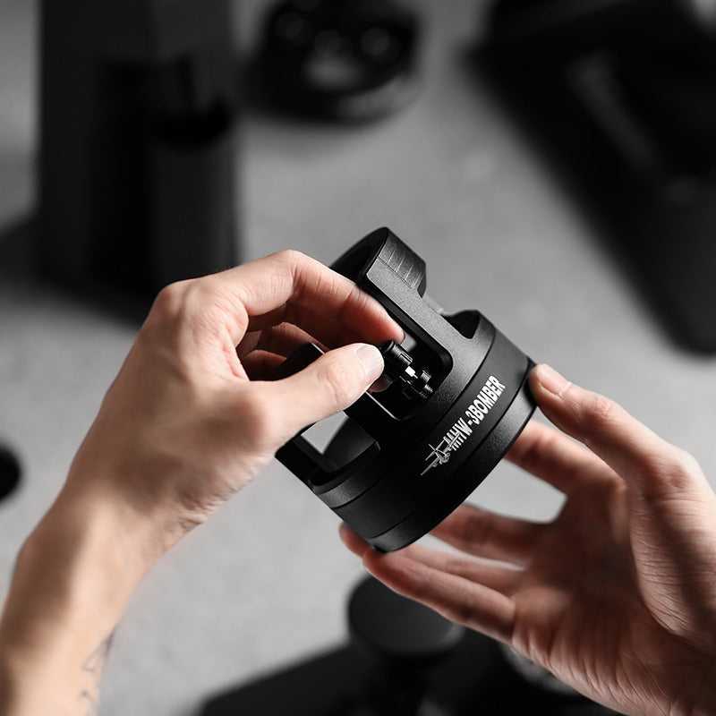 MHW-3BOMBER portafilter holder. Black, adjustable height coffee tamping station. Hands adjusting the device.