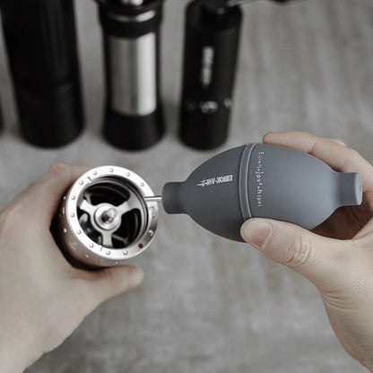 Coffee Air Blower being used to clean a grinder. Gray blower with stainless steel nozzle.