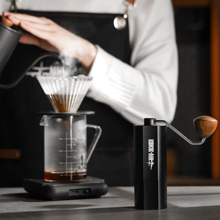 MHW-3BOMBER black manual coffee grinder with wood handle, point-to-point adjustment. Coffee being brewed.