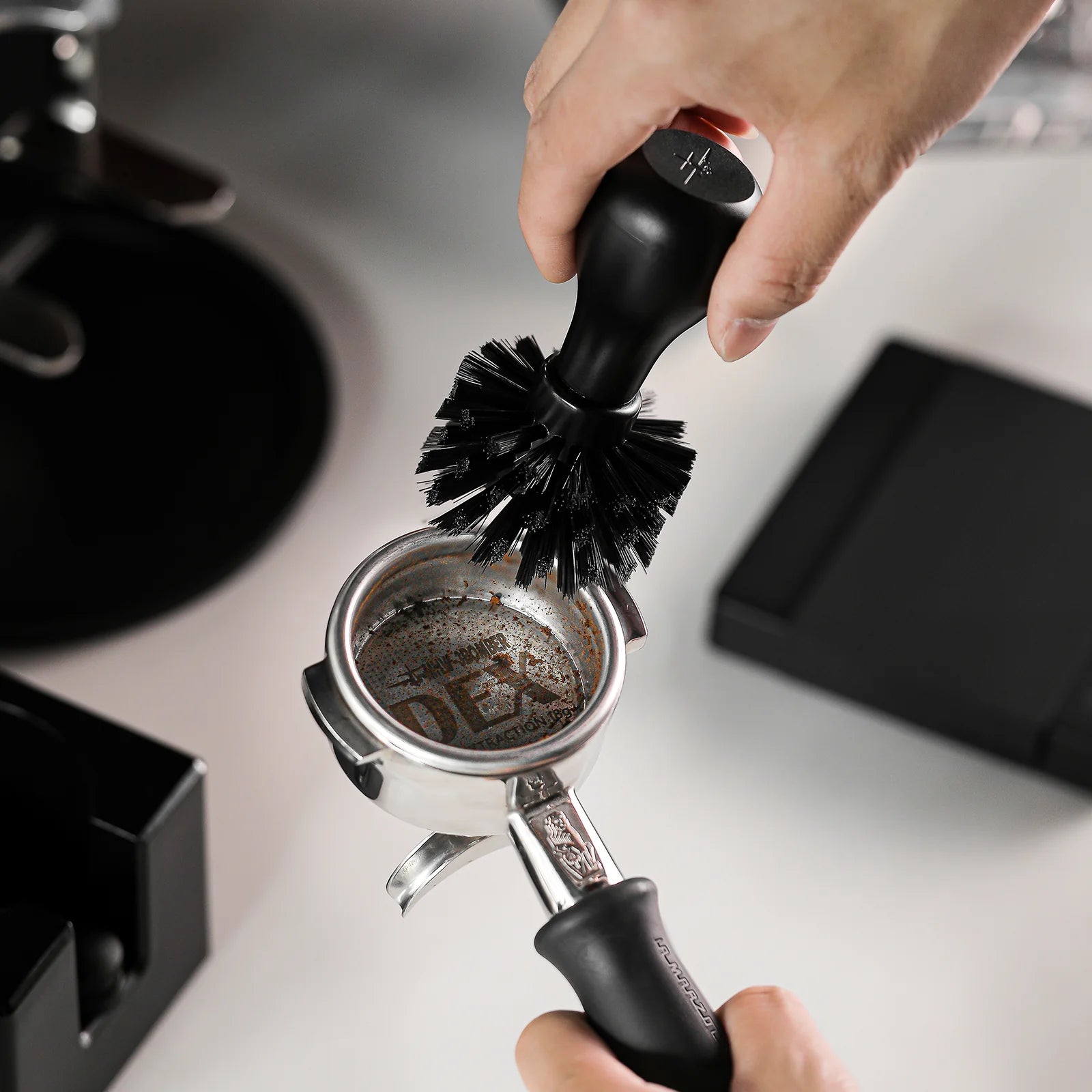 MHW-3BOMBER black coffee portafilter cleaning brush in use, removing coffee grounds. 
