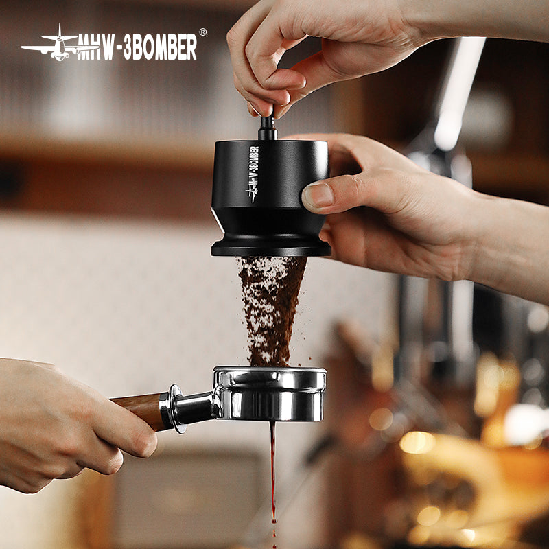 Close-up of hands using a black coffee grinder with fresh grounds flowing into a portafilter, enhanced by the MHW-3BOMBER Espresso Coffee Powder Dosing Funnel. A blurred kitchen background captures the scene beloved by baristas and home enthusiasts alike.