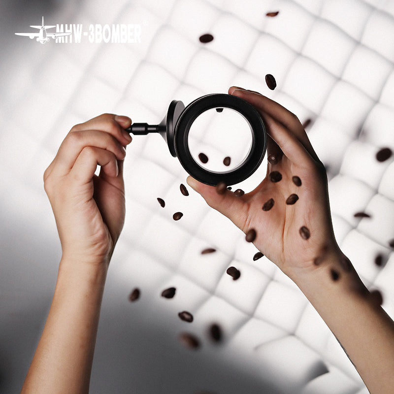 Hands hold a magnifying glass on a white quilted background surrounded by coffee beans, evoking barista imagery. The MHW-3BOMBER text in the top left showcases the Espresso Coffee Powder Dosing Funnel, appealing to both home enthusiasts and professionals.