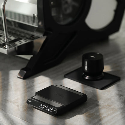 MHW-3BOMBER black smart espresso scale with timer and automatic liquid detection on a kitchen counter.