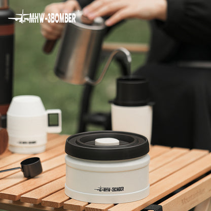 MHW-3BOMBER white vacuum coffee canister with black lid on a wooden table. Person pouring coffee in background.