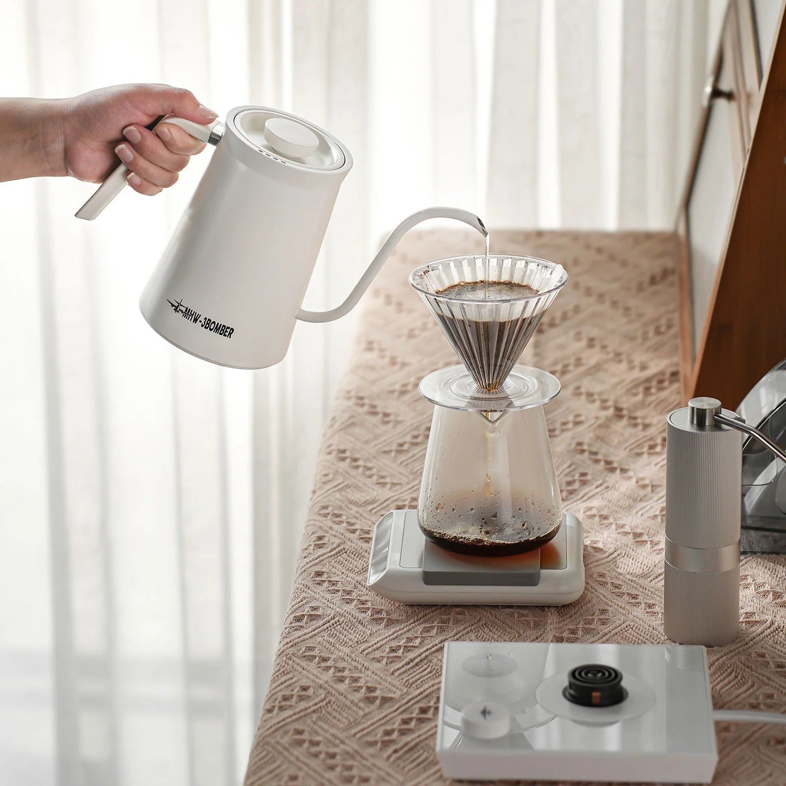 MHW-3BOMBER white gooseneck kettle pouring water into a glass pour-over coffee maker on a scale. 