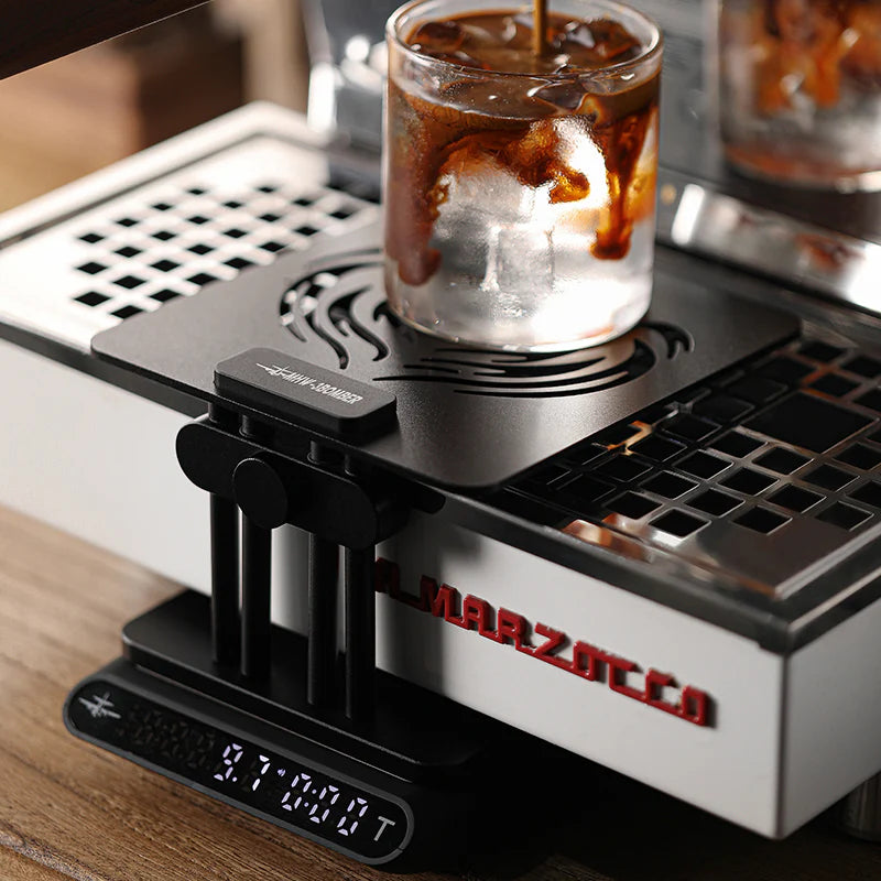 MHW-3BOMBER black coffee scale stand on a Marzocco espresso machine with iced coffee being poured.