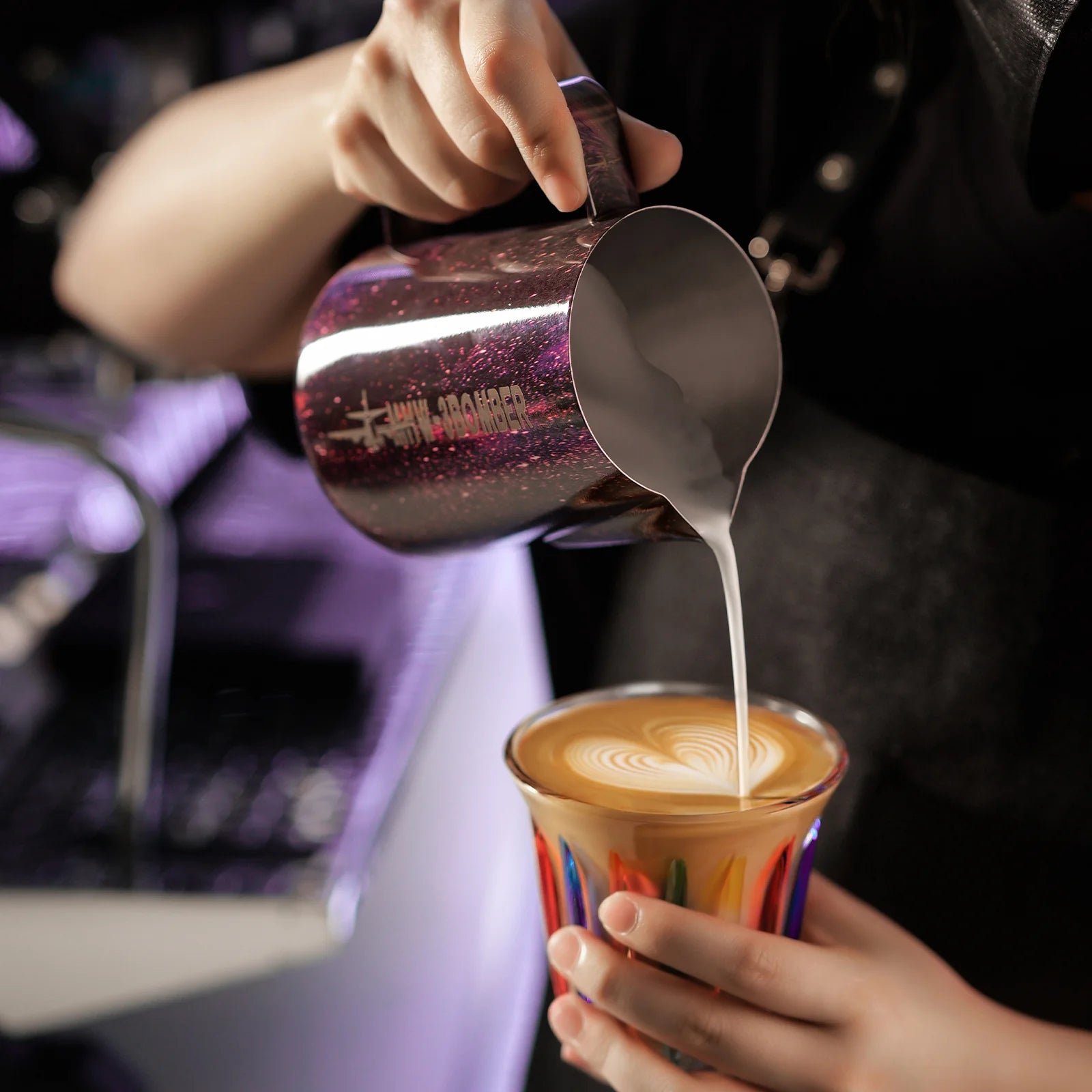 MHW-3BOMBER purple latte art pitcher pouring milk into a colorful cup with latte art. 