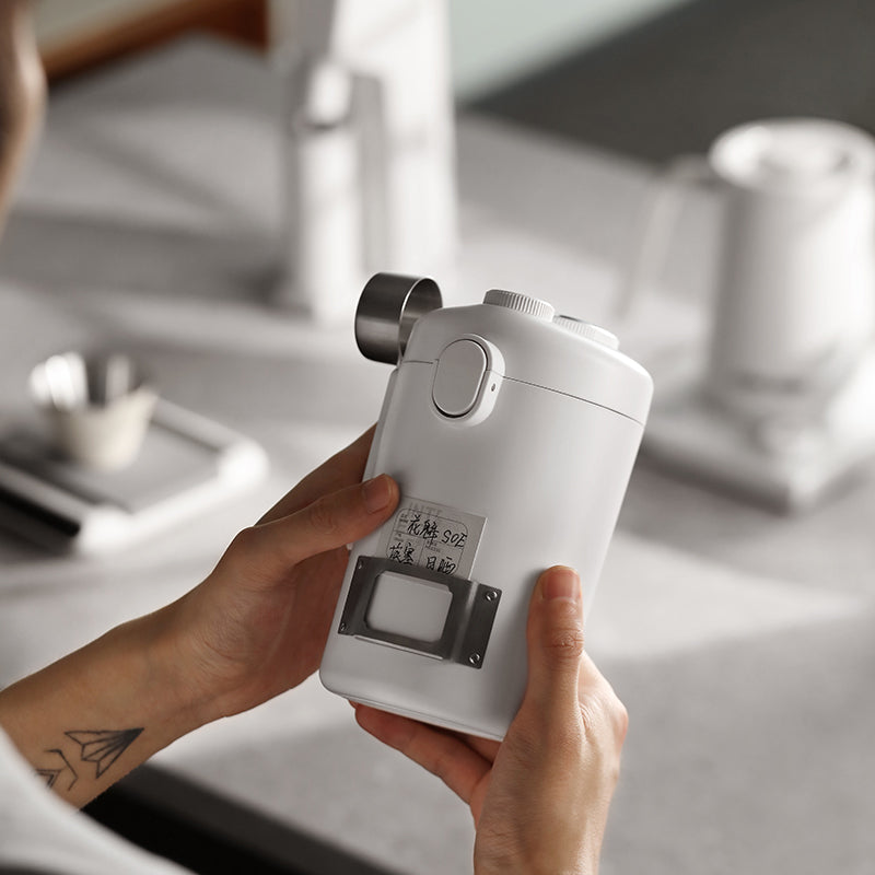MHW-3BOMBER white Gambo canister being held. Features: one-way valve, measuring spoon, date discs, metal board & labels.