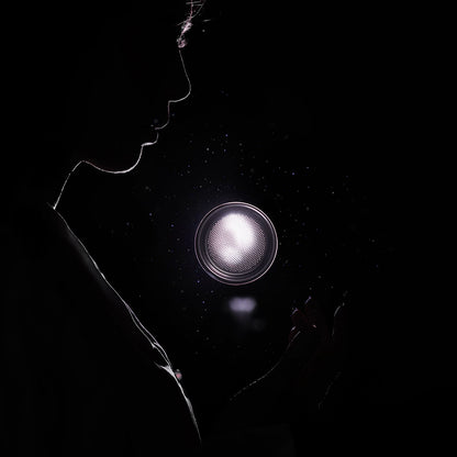 A silhouetted figure holds a glowing, circular light against a dark backdrop, resembling the gentle glow of the MHW-3BOMBER BEP Butterfly Coffee Filter Basket 2.0 58.5mm, with dust particles visible in the air.