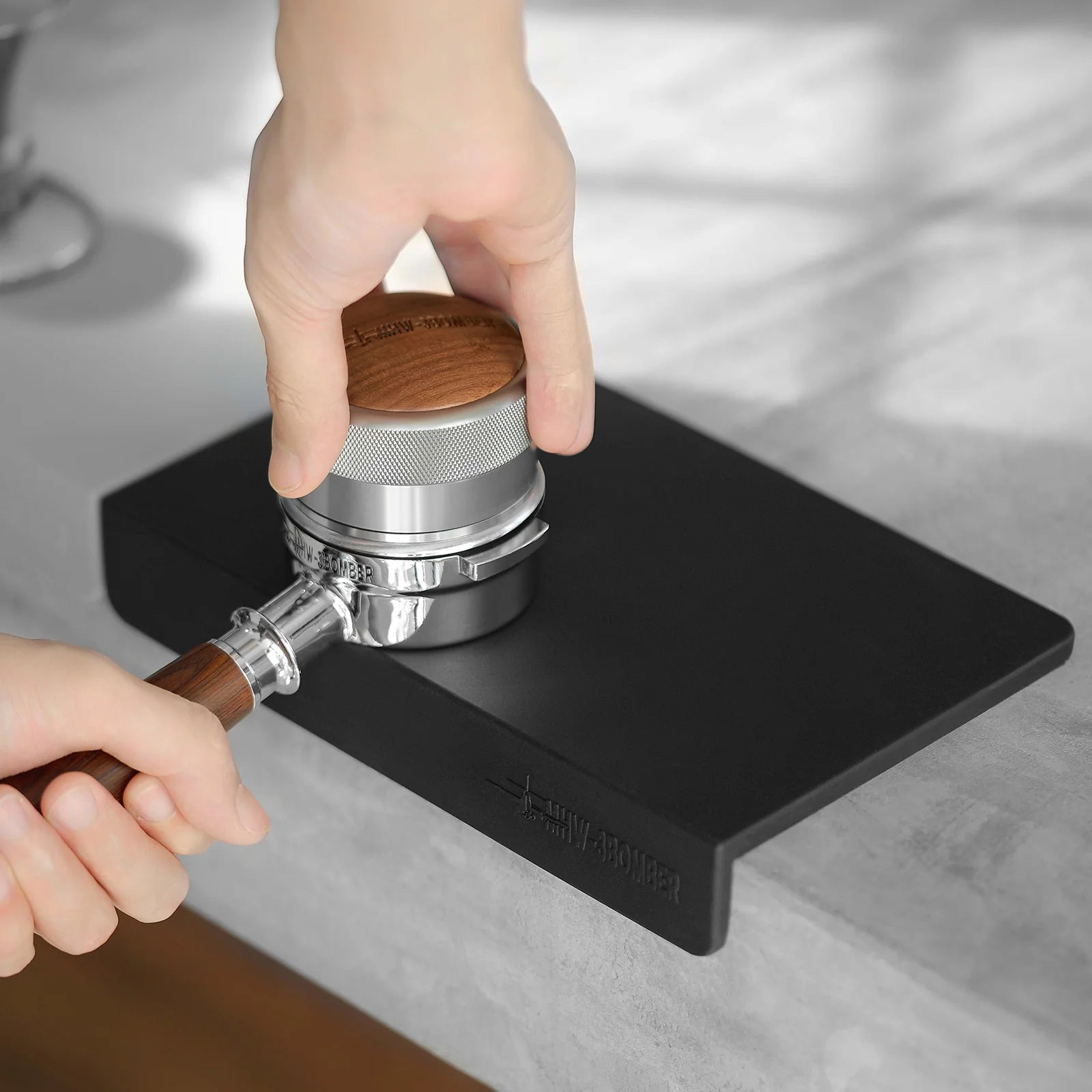 MHW-3BOMBER black silicone tamper mat with portafilter, for stable coffee tamping on the kitchen counter.