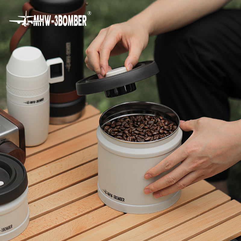 MHW-3BOMBER vacuum coffee canister filled with beans on a wood table. Person is closing the lid. 