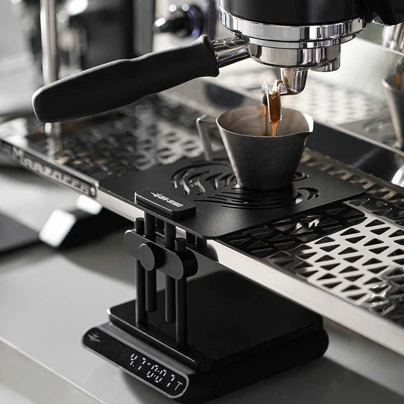 MHW-3BOMBER black coffee scale stand with adjustable height & non-slip base. Espresso pouring from machine above.