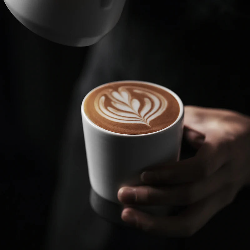 MHW-3BOMBER CERA white ceramic cup with latte art being held. U-shaped for aroma. Heat-resistant. 