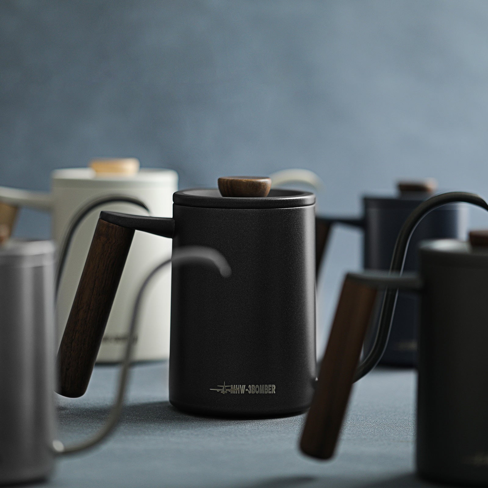 The MHW-3BOMBER Planet Hand Brewing Kettle collection, with sleek wooden-handled designs, elegantly features in a soft focus setting. A central black gooseneck kettle exemplifies minimalist aesthetics, perfect for drip coffee enthusiasts.