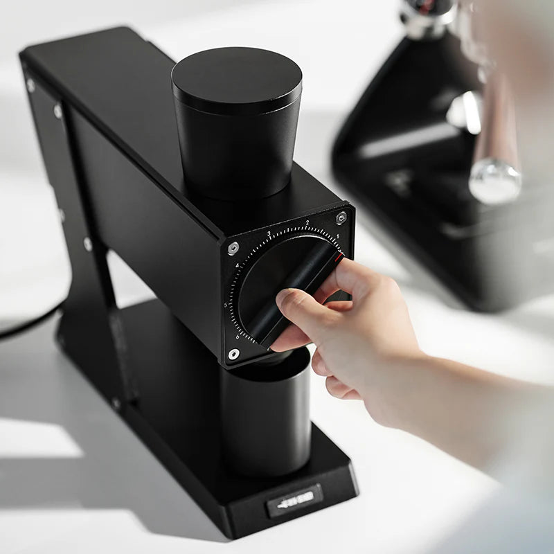 MHW-3BOMBER F74 grinder. Black coffee grinder with adjustable dial. Person's hand adjusting dial. 