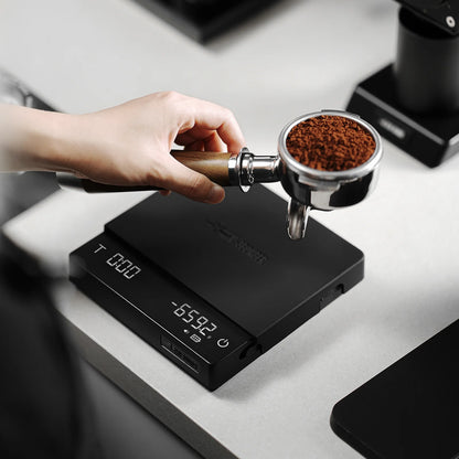 MHW-3BOMBER black cube coffee scale with portafilter and grounds on top. Digital display visible.