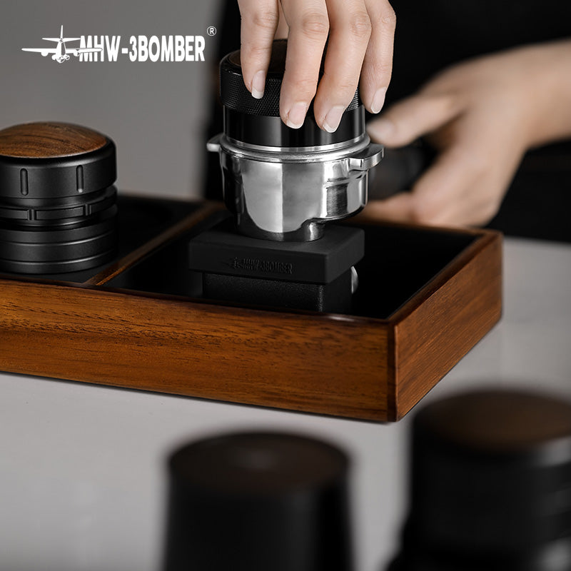 MHW-3BOMBER espresso tamping station with portafilter holder in wood, black silicone mat, and metal portafilter.