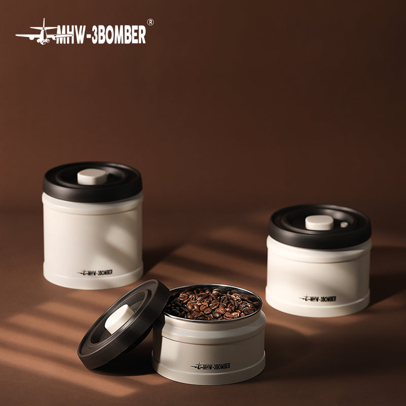 MHW-3BOMBER vacuum coffee canister. White & black design, with beans. Airtight storage for freshness.
