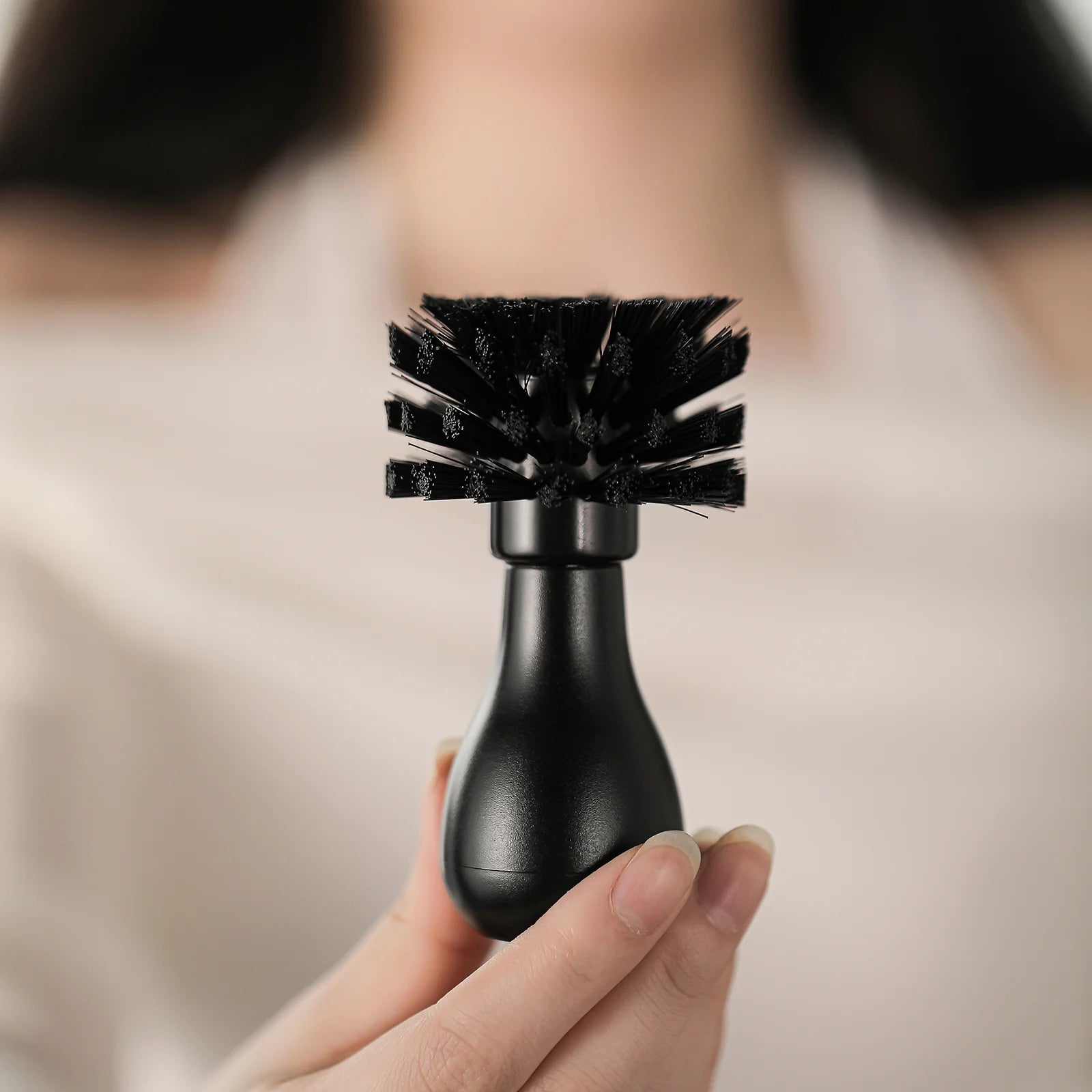 MHW-3BOMBER black portafilter cleaning brush for 58mm baskets, held in hand. Arc-shaped nylon bristles.