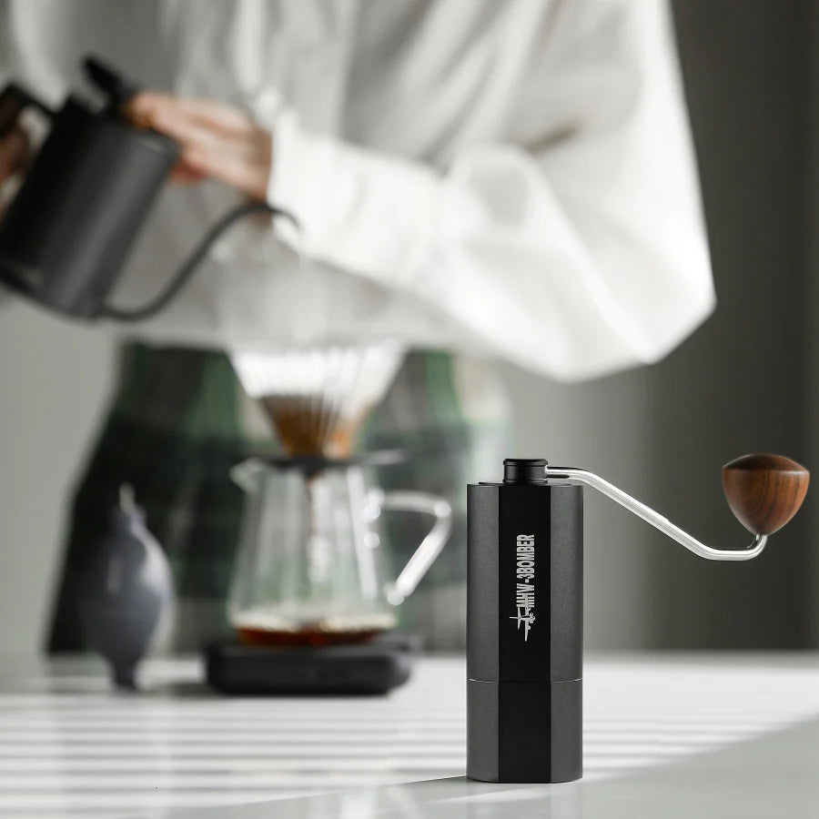 MHW-3BOMBER black manual coffee grinder with wooden handle. Shown in use with pour over setup. 