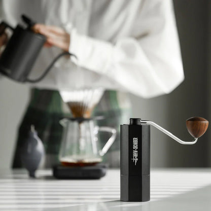 MHW-3BOMBER black manual coffee grinder with wooden handle. Shown in use with pour over setup. 