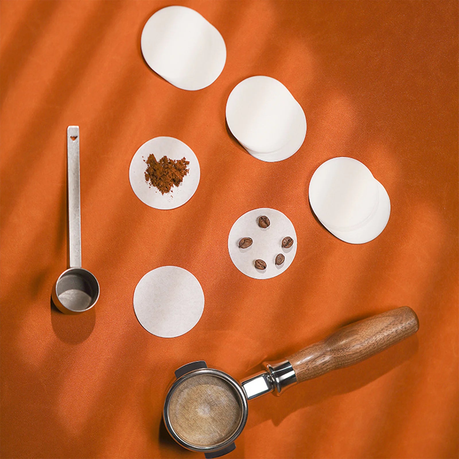 MHW-3BOMBER coffee filters, white paper, 51/53/58mm. Unbleached, round, on orange surface with scoop and portafilter.