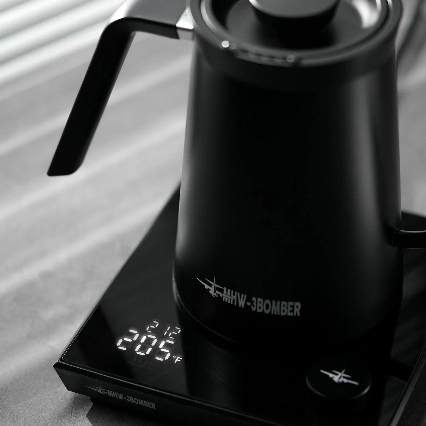 MHW-3BOMBER black gooseneck kettle on digital scale displaying 205°F. Precise pour control, stainless steel. 