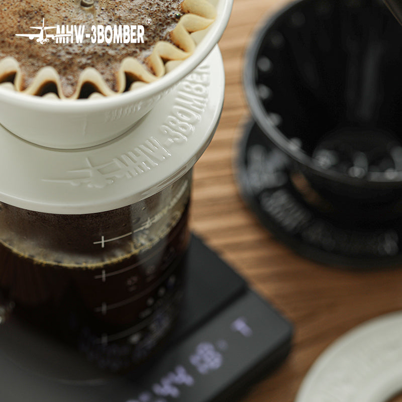 MHW-3BOMBER Meteor coffee dripper on scale. White ceramic pour-over brewing. Black coffee in glass container.