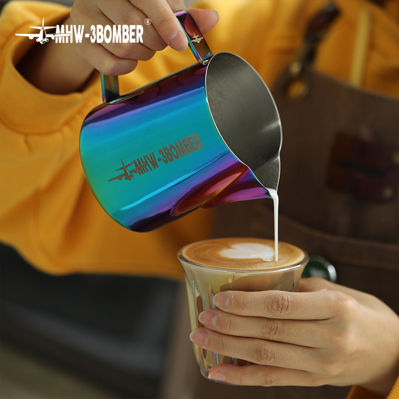 A person in a yellow shirt and brown apron skillfully pours milk from an MHW-3BOMBER Latte Art Pitcher 5.0 Colorful, featuring a crocodile spout, into a glass cup of coffee, adding flair to the scene.