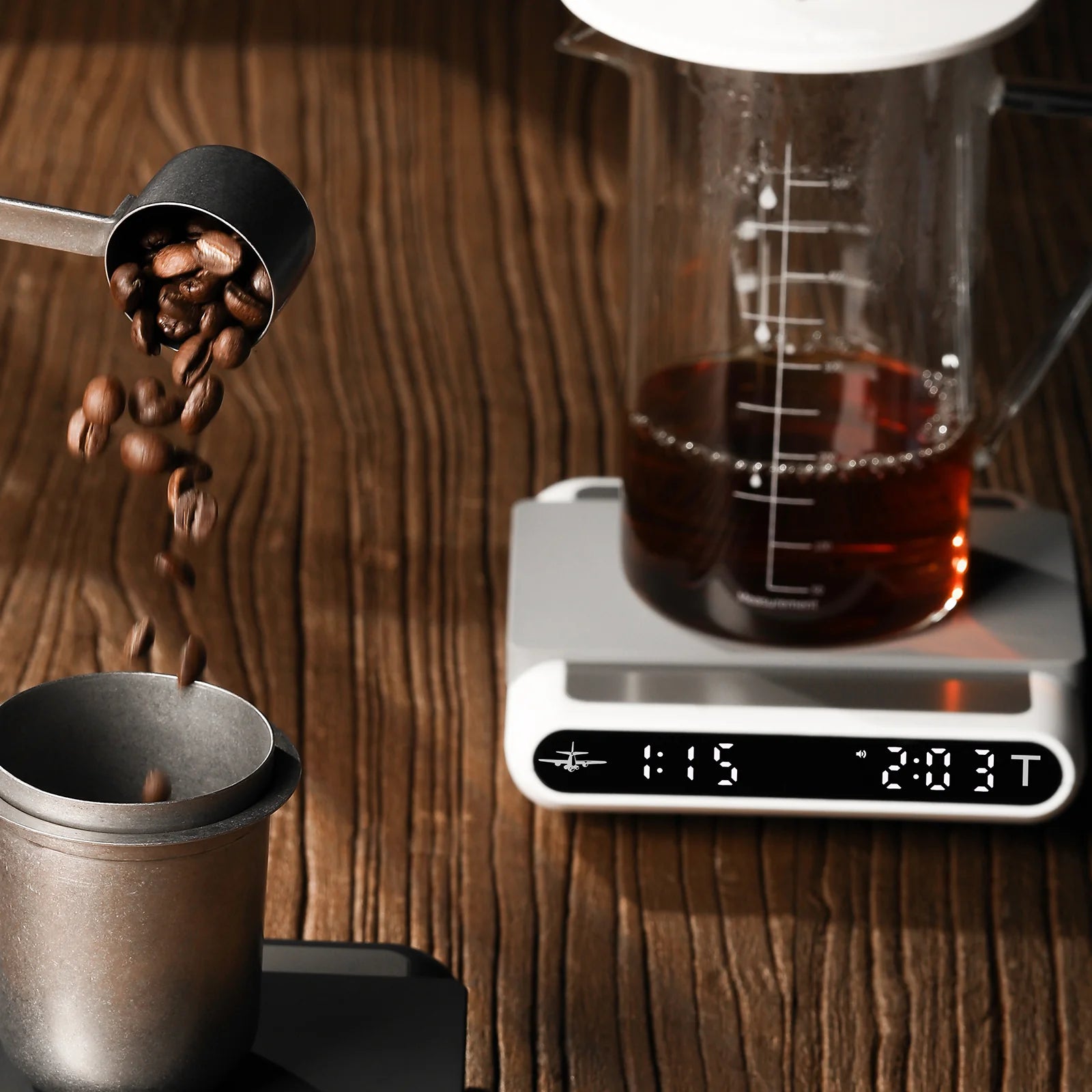 MHW-3BOMBER smart coffee scale with timer & beaker. Coffee beans falling. On a wooden surface.