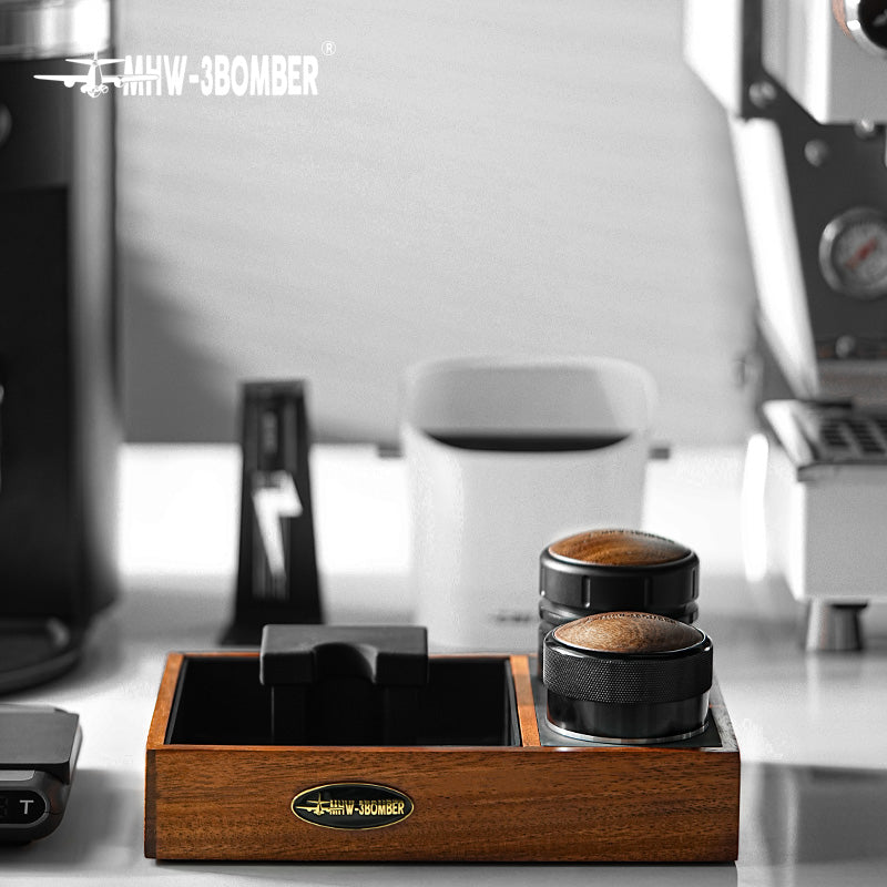 MHW-3BOMBER espresso tamping station with portafilter holder & tamper on counter. Wooden organizer, black details.