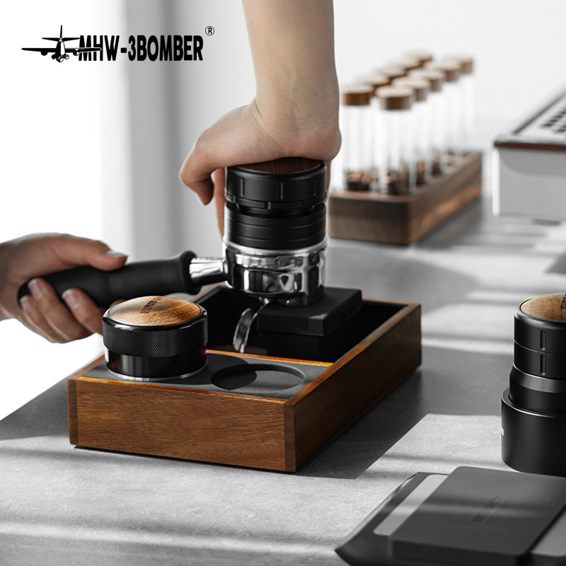 MHW-3BOMBER Espresso Tamping Station with wood base, black tamper, and portafilter. Coffee prep on counter.