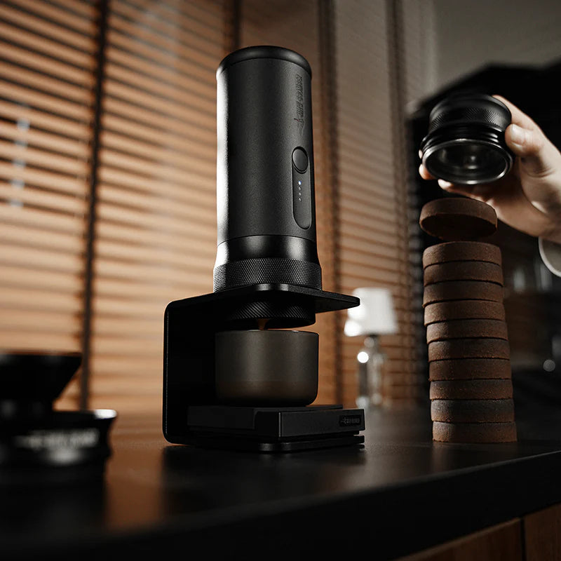Black coffee grinder with a stack of coffee grounds on a wooden surface.