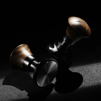 Two MHW-3BOMBER Armor Series Coffee Tamper 2.0 units with wooden handles rest on a dark surface, dramatically lit. Their bases have a shiny spiral pattern and they provide precision with adjustable tamping depth for consistent pressure in every brew.