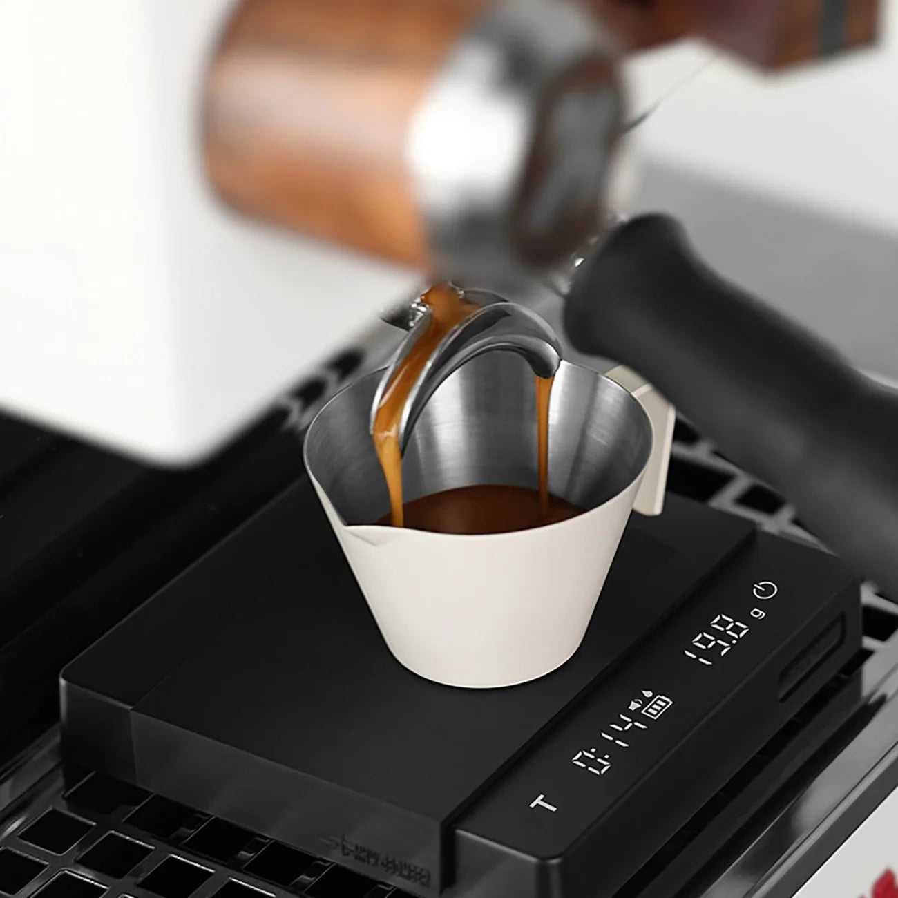 Espresso pours from a portafilter with a wooden handle into a metal cup on the MHW-3BOMBER Espresso Scale Cube Coffee Scale 2.0, displaying weight and time. This setup is part of an advanced coffee brewing machine renowned for meticulous accuracy.
