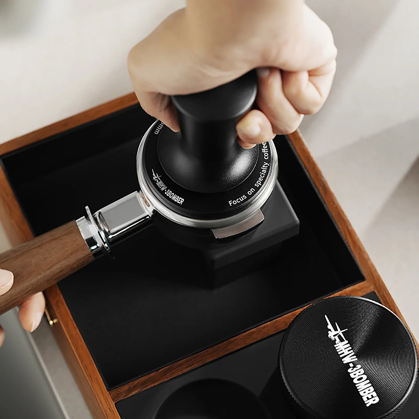 MHW-3BOMBER black CD Series coffee tamper with ripple base in use on wood tray. 