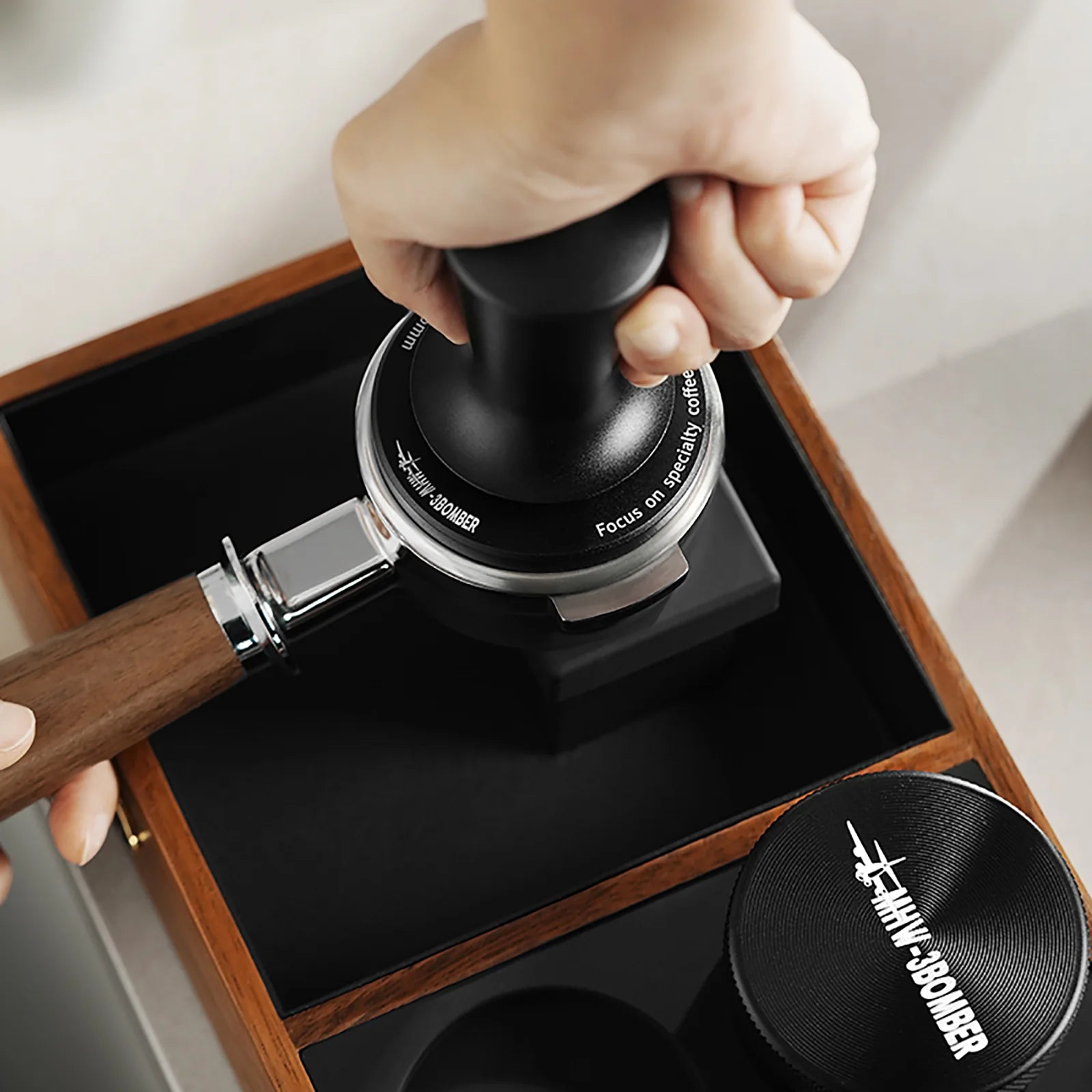 MHW-3BOMBER black CD Series coffee tamper with ripple base in use on wood tray. 