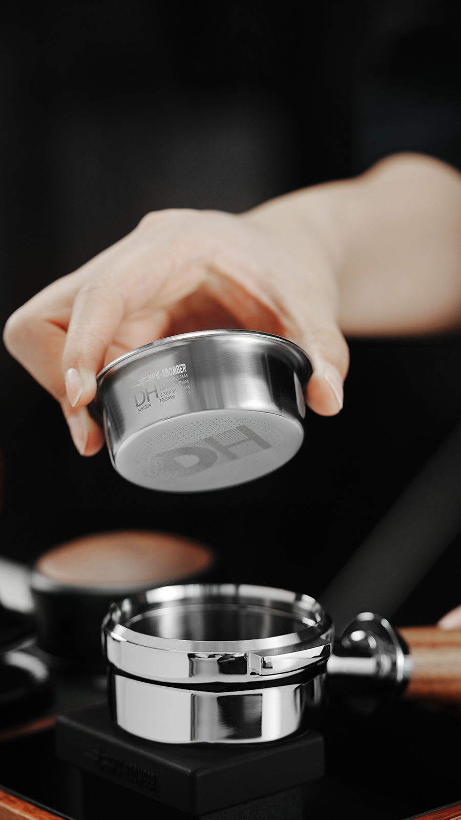 MHW-3BOMBER DH Filter Basket 58mm. Stainless steel coffee filter basket being held by a hand.