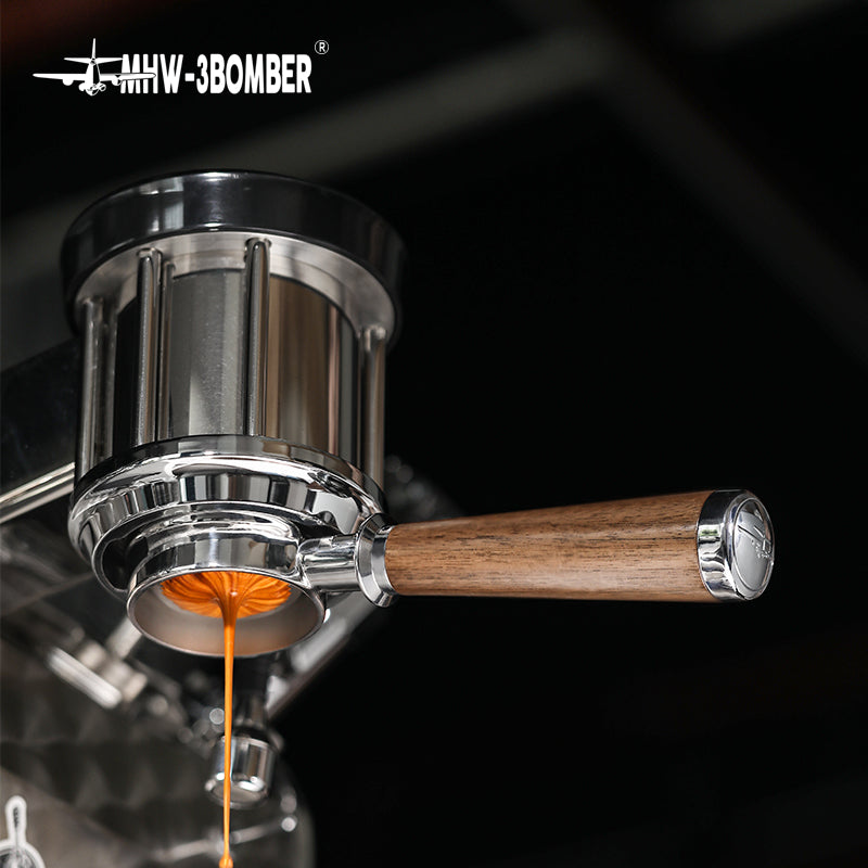 Close-up of an espresso machine with a natural walnut wood handle and coffee streaming into a cup below. The sleek, stainless steel design showcases the brand MHW-3BOMBER in the top corner, featuring their Bottomless Portafilter to enhance the brewing experience.