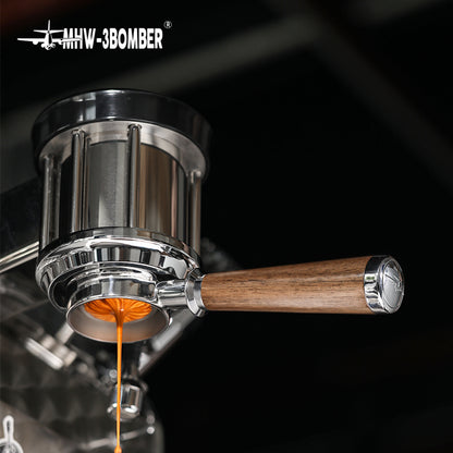 Close-up of an espresso machine with a natural walnut wood handle and coffee streaming into a cup below. The sleek, stainless steel design showcases the brand MHW-3BOMBER in the top corner, featuring their Bottomless Portafilter to enhance the brewing experience.