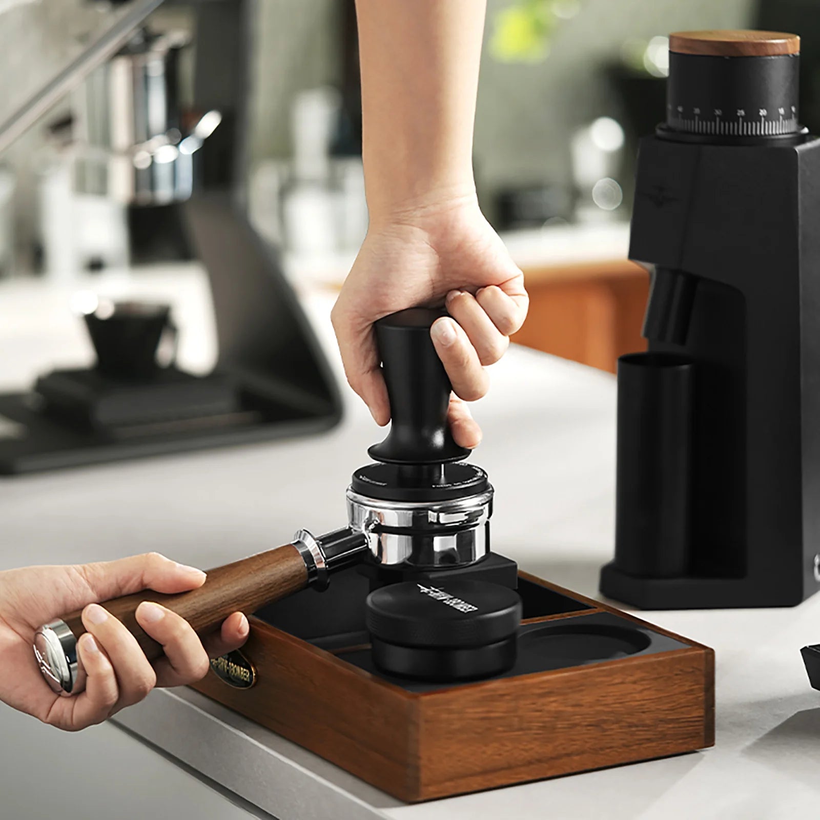 MHW-3BOMBER black tamper with ripple base being used on a wooden tamping station on a white counter.