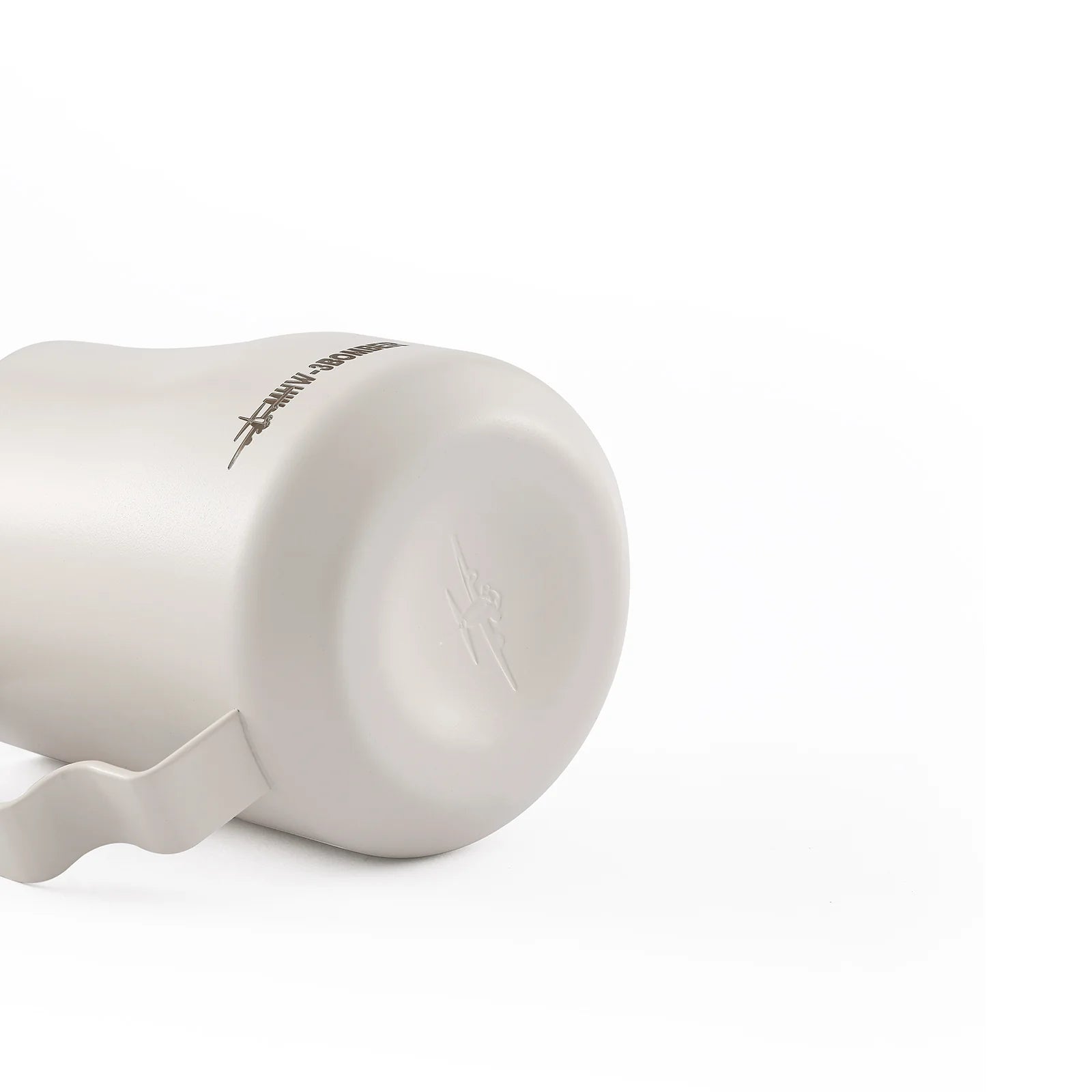 A stainless steel MHW-3BOMBER Turbo Milk Pitcher White lies on its side against a white background, ideal for milk frothing and latte art. It features a handle and has an embossed design with text near the base.