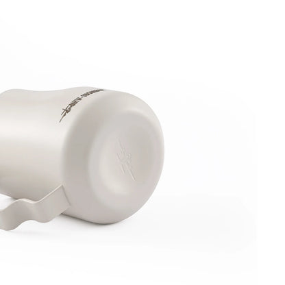 A stainless steel MHW-3BOMBER Turbo Milk Pitcher White lies on its side against a white background, ideal for milk frothing and latte art. It features a handle and has an embossed design with text near the base.