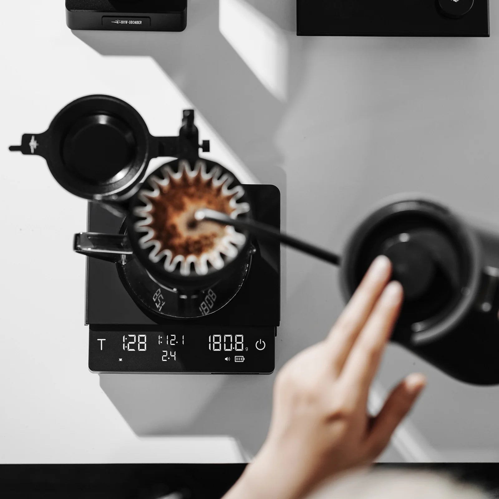 MHW-3BOMBER Cube Coffee Scale 3.0 Pro Max in use. Black scale with digital display showing weight and time. 