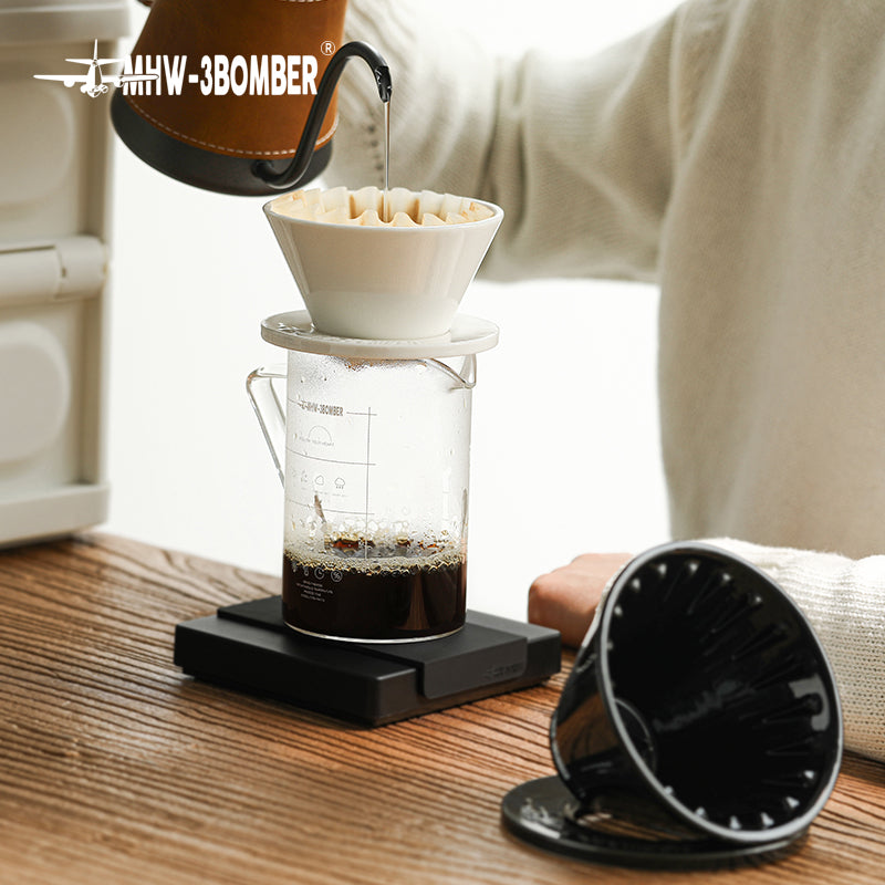 MHW-3BOMBER Meteor coffee dripper in use. White ceramic dripper on clear glass server. Black filter holder visible.